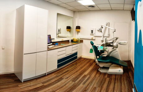 Box 2 Fotografia d'un box d'un dentista on hi ha mobles blancs amb dues calaixeres de color negre, al damunt un espill quadrat gran i una cadira odontològica.