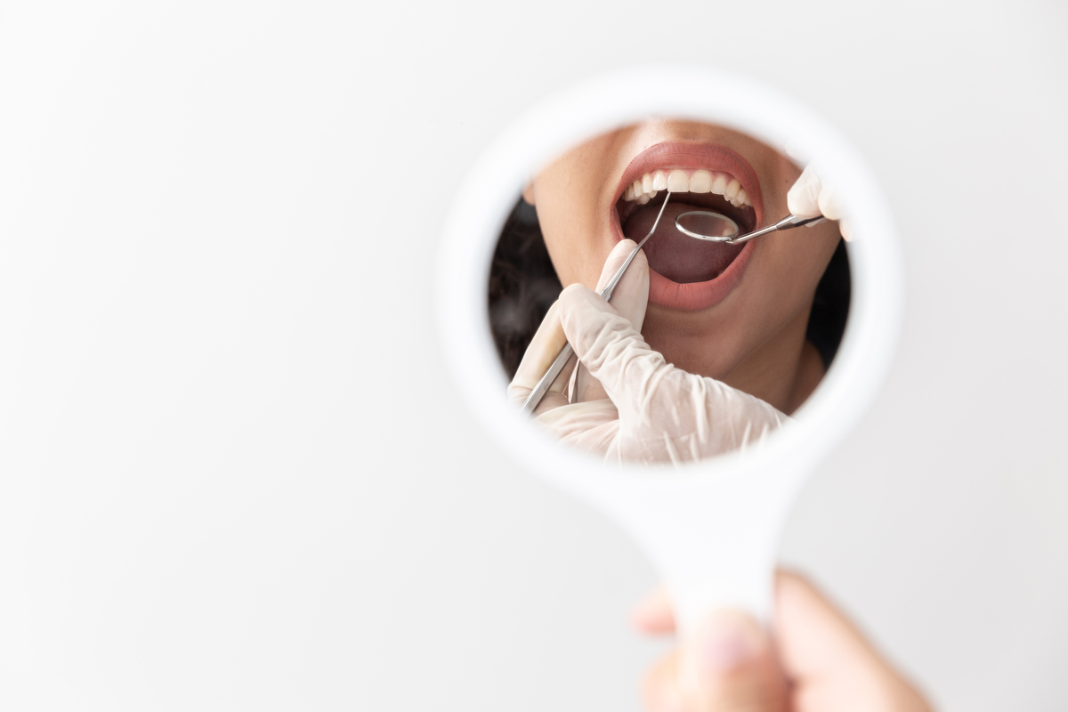 Fotografia d'un mirall on es veuen les mans d'un dentista amb guants fent una revisió oral a un pacient.