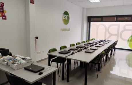 Aula amb taules i cadires i llibres al damunt.